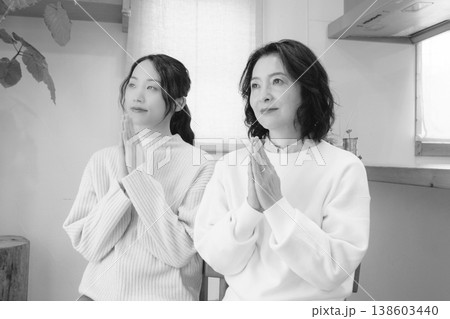 自宅で故人に祈りを捧げる母と娘（モノクロ） 138603440