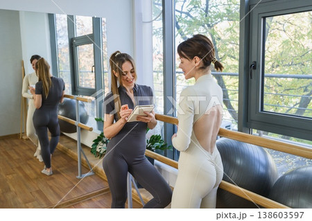 Female trainer taking notes while talking to client in fitness studio. Female trainer taking notes while talking to client in fitness studio. 138603597