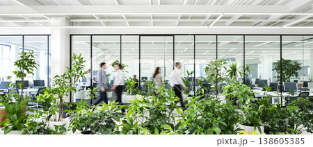 Photo of a modern open office space with indoor plants and blurred people walking, promoting a healthy and productive work environment. 138605385