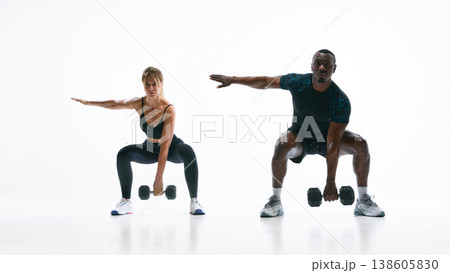 Athletic couple performing squat with dumbbells in functional strength training workout. Athletic couple performing squat with dumbbells in functional strength training workout. 138605830