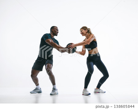 Fitness couple passing medicine ball in functional training workout on white background Fitness couple passing medicine ball in functional training workout on white background 138605844