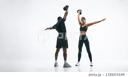 Athletic couple performing rotational kettlebell exercise isolated on white. Athletic couple performing rotational kettlebell exercise isolated on white. 138605846