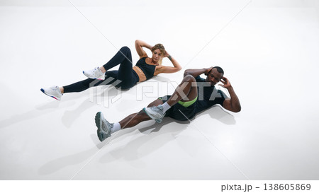 Fitness couple doing bicycle crunch exercise isolated on white background. Fitness couple doing bicycle crunch exercise isolated on white background. 138605869