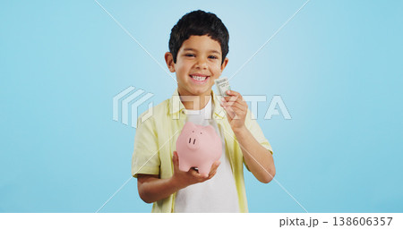 Piggy bank, cash and child face with money, savings and cash planning in a studio, Happy, portrait and young boy with allowance and safe for bills, wealth and budget with blue background and smile 138606357