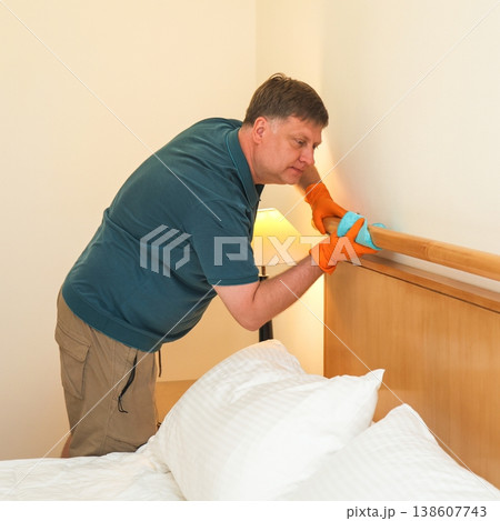 The husband cleans the bedroom, carefully wipes dust from the headboard, creating a fresh and cozy home atmosphere for his family The husband cleans the bedroom, carefully wipes dust from the headboard, creating a fresh and cozy home atmosphere for his family 138607743