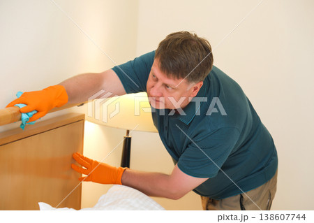 The husband cleans the bedroom, carefully wipes dust from the headboard, creating a fresh and cozy home atmosphere for his family 138607744