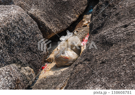 Plastic bags with waste trapped between coastal rocks on Koh Samui beach, highlighting pollution and environmental impact in tropical seaside area 138608781