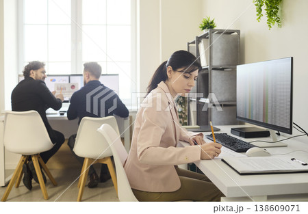 Focused woman working at computer, men collaborating in modern office workspace Focused woman working at computer, men collaborating in modern office workspace 138609071