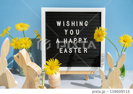 WISHING YOU A HAPPY EASTER text on letter board with bunny wooden figures and fresh flowers. Easter composition content still life. Christian symbols of spring 138609518