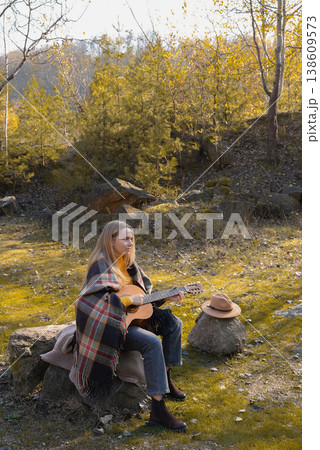 Portrait of smiling caucasian artist plays wooden acoustic guitar in autumnal park. Young songwriter plays string musical instrument hobby outside in nature fall time. Audio music healing Portrait of smiling caucasian artist plays wooden acoustic guitar in autumnal park. Young songwriter plays string musical instrument hobby outside in nature fall time. Audio music healing 138609573