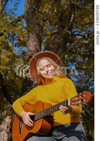 Blonde woman playing string guitar outdoors in autumn forest. Concept of sound therapy, mental health and wellness rituals. Calmness tranquility audio-sensory practices. Aura farming energy Blonde woman playing string guitar outdoors in autumn forest. Concept of sound therapy, mental health and wellness rituals. Calmness tranquility audio-sensory practices. Aura farming energy 138609586