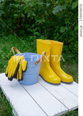 Gardening tools on outdoor greenery background. Concept of homegrown farm healthy living. Yellow boots with bucket and garden gloves  138609658
