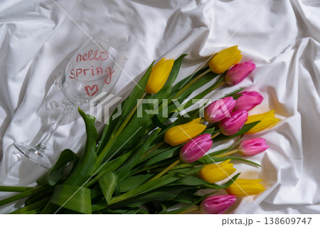 Bouquet of colorful tulips on messy bed. HELLO SPRING written text on wine glass. Romantic morning scene. Greeting card Holiday flowers springtime 138609747