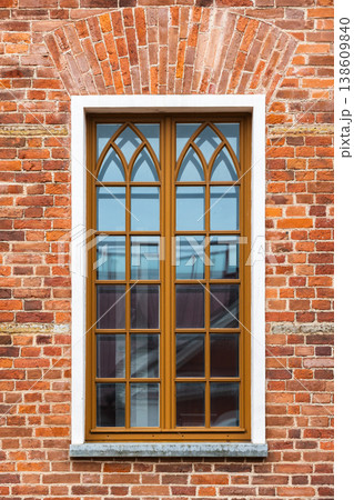 An arched wooden window sits in a red brick wall 138609840