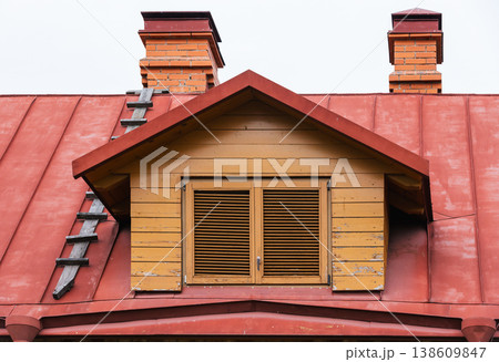 Yellow wooden dormer with closed louvered window set on a red metal roof Yellow wooden dormer with closed louvered window set on a red metal roof 138609847