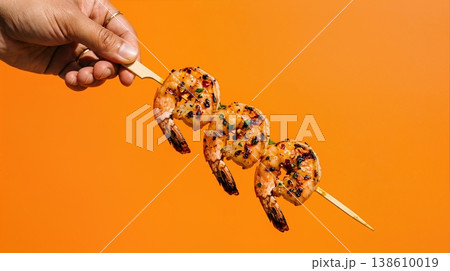 Hand Holding Grilled Shrimp Skewer with Chili Oil Glaze Isolated on a Solid Bright Orange Background 138610019
