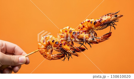 Hand Holding Grilled Shrimp Skewer with Chili Oil Glaze Isolated on a Solid Bright Orange Background 138610020