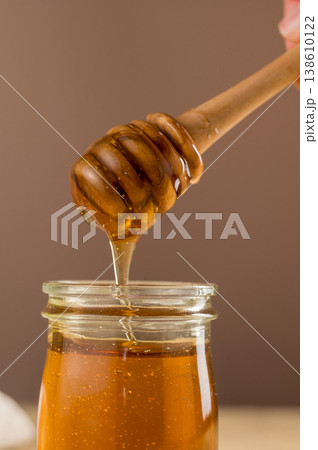 Jar of honey with wooden dipper, sweet liquid, neutral background 138610122