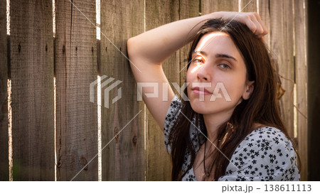 Young woman looking at camera beside wooden fence 138611113
