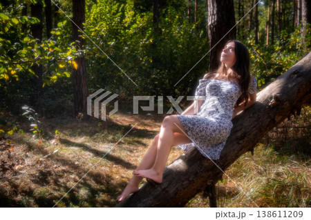 Young woman looking up while sitting on tree trunk outdoors 138611209