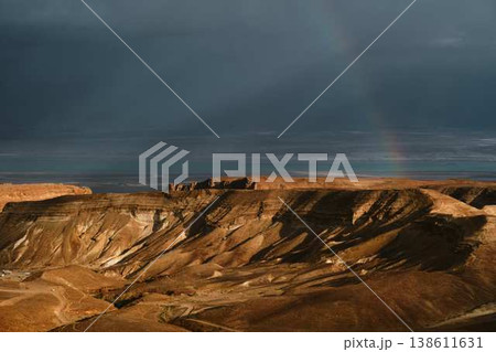 Dramatic rainbow over desert landscape with storm clouds and sea view Dramatic rainbow over desert landscape with storm clouds and sea view 138611631