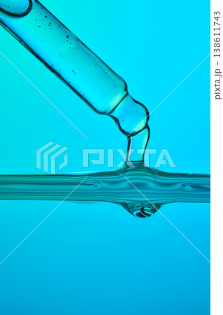 Pipette dropping liquid into blue water surface 138611743