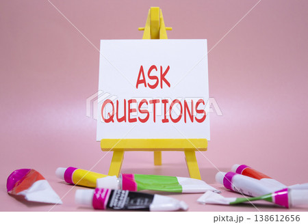 Ask Questions symbol. Wooden blocks with words Ask Questions. Beautiful pink background with paints and easel. Business and Ask Questions concept. Copy space. 138612656