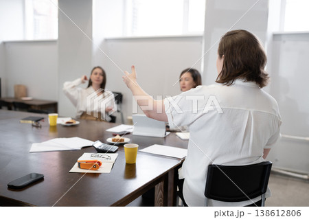 Woman giving presentation and gesturing as others listen during business breakfast at office table. Presentation, gesturing, business, breakfast, office, teamwork. 138612806