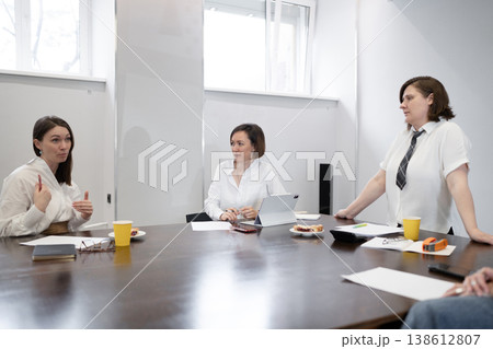 Female business partners seated and communicating at meeting table during group breakfast in office. Partners, breakfast, group, meeting, communicating, office. 138612807