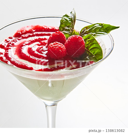 Gourmet panna cotta served in a martini glass with a vibrant raspberry coulis swirl and fresh mint 138613082
