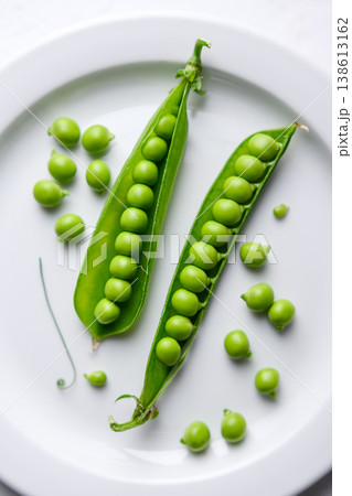 Fresh green peas scattered on a white plate with open pods 138613162