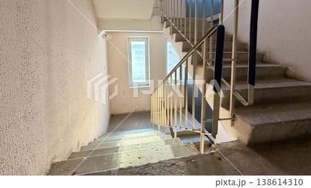 Apartment building stairwell with concrete stairs going down, metal railings and sunlight through window. Apartment building stairwell with concrete stairs going down, metal railings and sunlight through window. 138614310