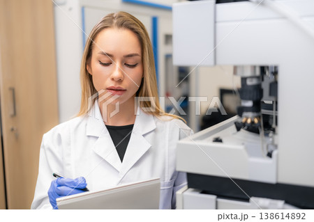 Laboratory technician recording data during analysis of samples at a clinical research facility. The workspace features modern analytical instruments and a clean, organized environment. Laboratory technician recording data during analysis of samples at a clinical research facility. The workspace features modern analytical instruments and a clean, organized environment. 138614892