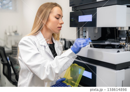 Laboratory technician inserting HPLC vials into advanced analytical equipment for testing in a pharmaceutical lab. 138614898