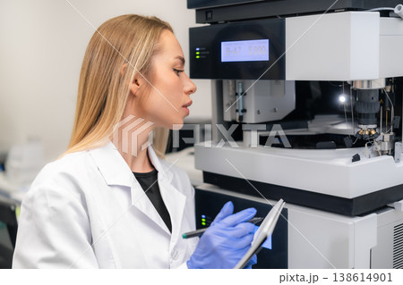 Laboratory technician configuring advanced analytical instrument HPLC at pharmaceutical research workstation. Clean environment with digital display and precision tools visible in background. Laboratory technician configuring advanced analytical instrument HPLC at pharmaceutical research workstation. Clean environment with digital display and precision tools visible in background. 138614901