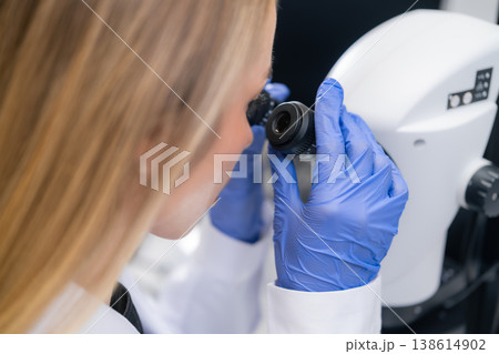 A technician examines a sample using a high resolution digital microscope in a sterile laboratory setting. A technician examines a sample using a high resolution digital microscope in a sterile laboratory setting. 138614902