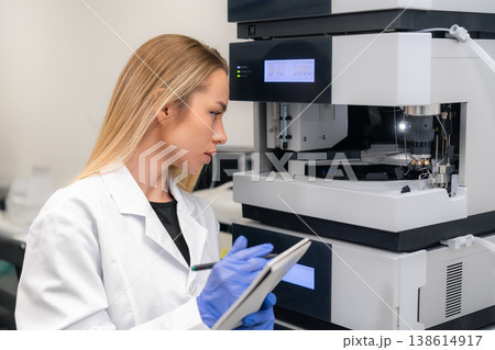 A technician calibrates a high performance liquid chromatography HPLC system at a laboratory workstation. The clean environment features advanced analytical equipment and digital readouts. 138614917