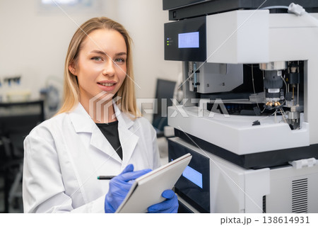 Laboratory technician documenting data while operating sophisticated analytical equipment HPLC in clinical environment. Bright workspace with modern technology and precision tools visible in 138614931