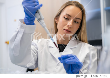 Performing precise pipetting technique to transfer red liquid samples into microcentrifuge tubes at laboratory workstation. Blood sample analysis 138614950
