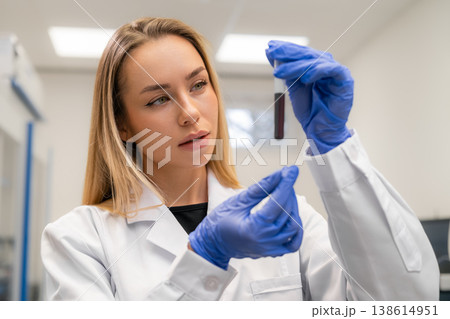 Laboratory technician analyzing blood sample contained in a glass test tube at a clinical workstation. 138614951