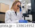 Laboratory technician examining cellular samples through advanced microscope in research facility. Clean and organized environment with high tech equipment visible in background. 138614952