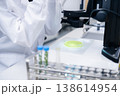 Laboratory scientist analyzing green agar cultures on glass slide using a microscope. Clean workspace with organized test tubes and precision instruments visible in background. Plant analysis concept 138614954