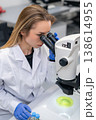 A professional researcher examines green biological samples through a high quality microscope at a laboratory workstation. 138614955