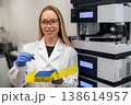 Clinical technician operating precision automated HPLC analyzer while holding amber vial and yellow microcentrifuge tube rack at laboratory workstation. 138614957