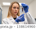 Laboratory technician analyzing a blood sample contained within a test tube at a clinical research facility. Clean, well lit environment with sterile surfaces and laboratory equipment visible. 138614960
