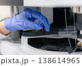 Technician operating automated liquid handling system HPLC, inserting an amber vial with a blue cap into the analyzer. Clean laboratory environment featuring precision equipment and organized 138614965