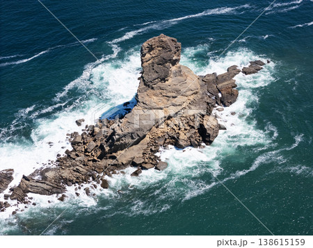 Rock formation in ocean with waves around it on sunny day 138615159