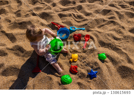 Toddler sitting on sandy beach playing with plastic bucket shovel and sand molds. Outdoor beach photography. Childhood and summer vacation concept. Design for poster, banner, postcard. Top view shot Toddler sitting on sandy beach playing with plastic bucket shovel and sand molds. Outdoor beach photography. Childhood and summer vacation concept. Design for poster, banner, postcard. Top view shot 138615693