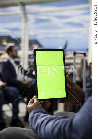 Vertical chroma key tablet in international airport terminal with diverse passengers relaxing in waiting lounge. Travelers with suitcases checking passports and plane tickets before journey. Vertical chroma key tablet in international airport terminal with diverse passengers relaxing in waiting lounge. Travelers with suitcases checking passports and plane tickets before journey. 138615818