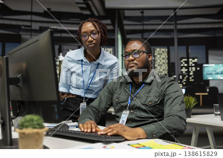 Two black colleagues engaged in project planning and report writing, using company data insights to ensure alignment with objectives. Reviewing reports on computer at the office. Two black colleagues engaged in project planning and report writing, using company data insights to ensure alignment with objectives. Reviewing reports on computer at the office. 138615829
